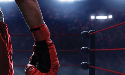 shot of boxing ring from behind a boxer in red shorts and boxing glove