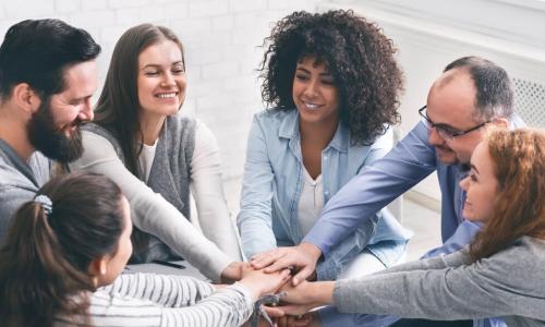 smiling circle of employee team members put hands together to support each other