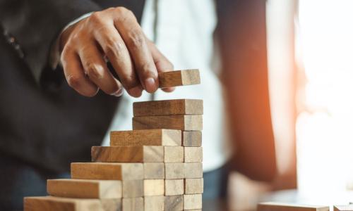 hand of businessman in suit building a growing staircase out of wooden blocks