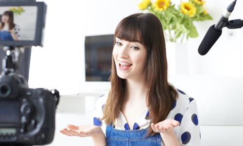 smiling young woman in polka dot shirt records video in front of camera and microphone