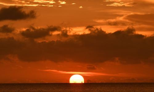 sun sinks below ocean horizon on cloudy evening
