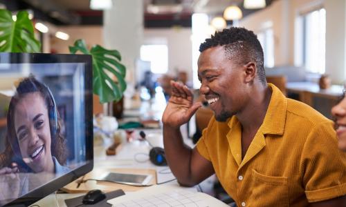 Smiling employees in office wave to coworker on screen during video conference call