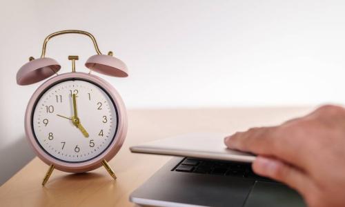 employee closes laptop on desk as alarm clock reaches 5 PM