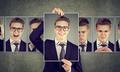 businessman choosing to hold up picture of positive personality from among other pictures expressing various emotions