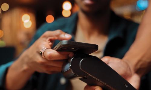 customer holds out smartphone to tap wireless payment device in a restaurant