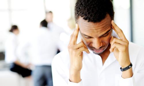 stressed new Black business leader rubs his temples while teammates talk in office background