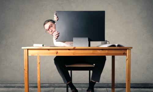 manager avoiding employees by hiding behind computer monitor at his desk