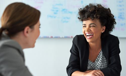 female colleagues in office laugh together during a meeting showing great rapport