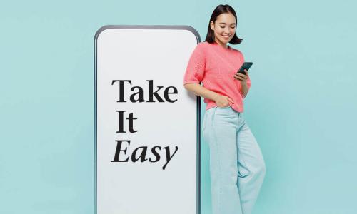 young woman in pink sweater using smartphone while standing next to a giant smartphone screen