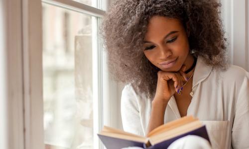 young African American businesswoman reading a book while sitting on window sill
