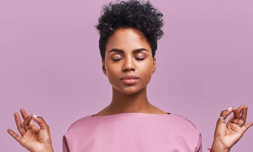 calm woman in purple shirt closes eyes and holds hands up in meditation pose 