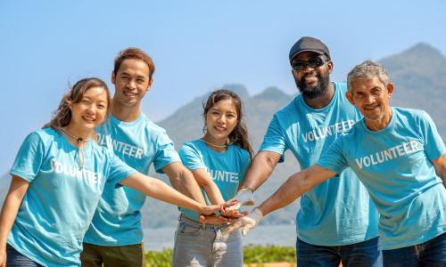 Diverse group of corporate volunteers stack hands together to kick off charitable volunteer project