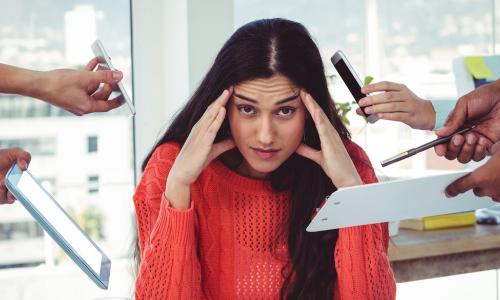 young business woman holds head as colleagues in the office hand her more and more work