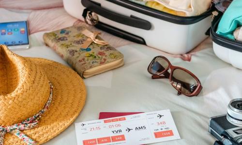 straw summer hat with plane ticket phone and camera next to open luggage