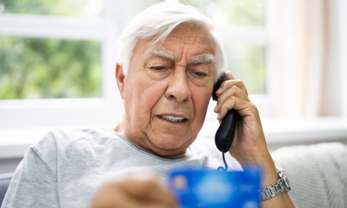 older man holds credit card while on the phone