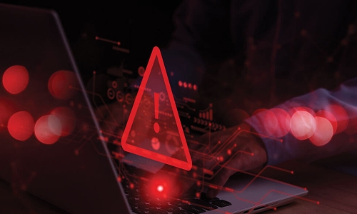 hands typing on laptop keyboard while large red warning triangle sign displays in front of screen