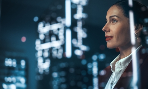 a successful businesswoman looks out at the lit up city skyline