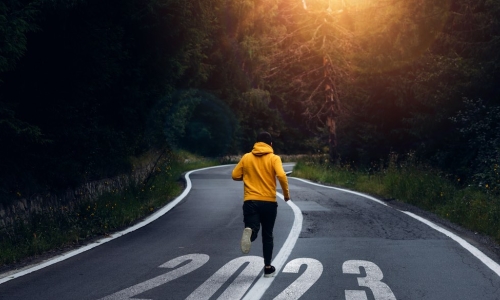 man in yellow hoodie jogging down road marked 2023 with bright sun peaking through the trees ahead