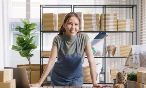 small business owner works on laptop while preparing packages for customers