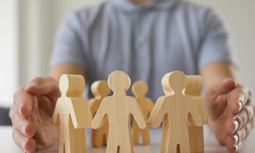 leader holds hands protectively around people figures representing workplace team