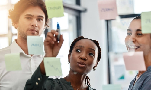 business leader points to board of sticky notes while working with employees