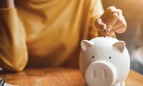 person in yellow sweater reaches out to drop a coin into a piggy bank