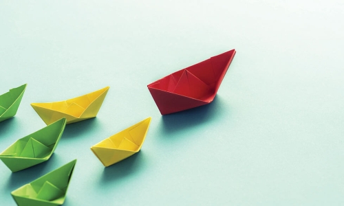 red paper boat leads a team of yellow boats leading a bigger team of green boats across the page