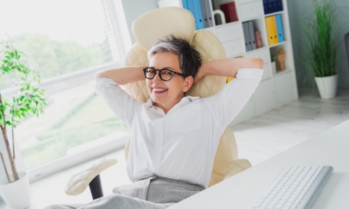 Photo of cheerful older businesswoman with her hands over her head at a desk isolated in an office