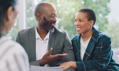 A smiling black couple sits across a desk from another person