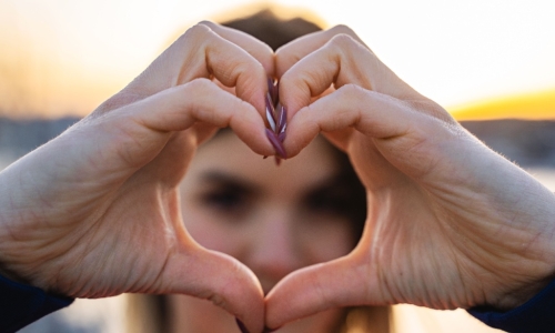 A young Gen Z woman creates a heart shape with her hands