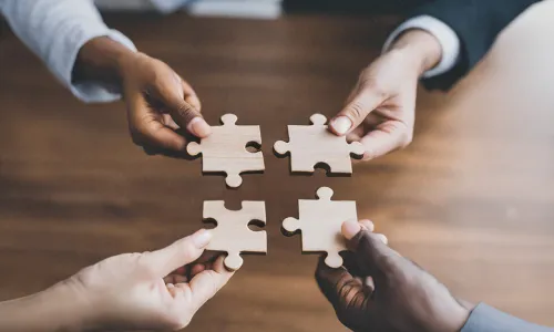 four hands holding puzzle pieces bringing them all together in the center