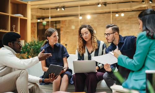 Group of individuals sitting around a coffee table looking at laptops and papers having a meeting