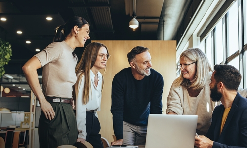 5 individuals standing around a table looking at a laptop