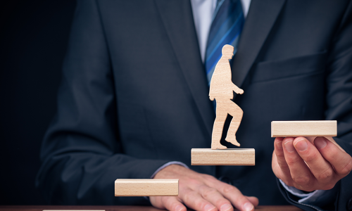 man holding wooden blocks creating stairs for wooden man to climb