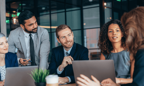 individuals sitting around a table looking over a laptop