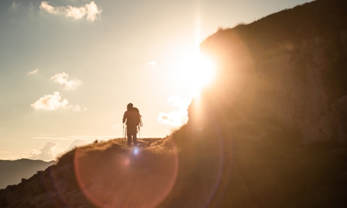 man climbing mountain walking into the sun