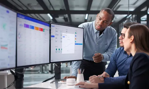 individuals looking at a 3 monitor set up while talking