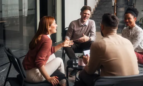 4 individuals sitting on a patio around a table laughing and talking