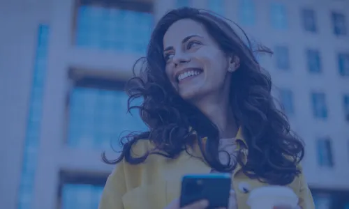 woman holding cell phone and coffee smiling over her shoulder