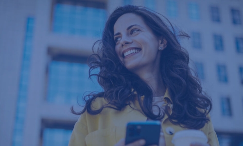 woman holding cell phone and coffee smiling over her shoulder