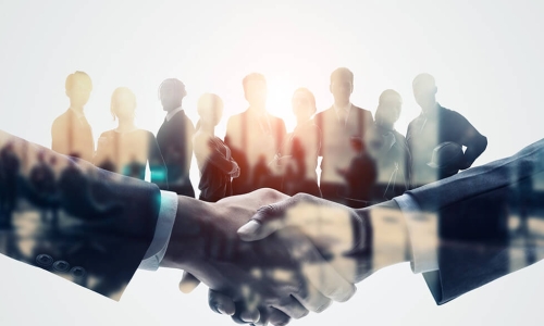 close up of a handshake with silhouette of individuals behind the joined hands